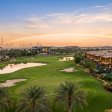 Aerial view of Jumeirah Golf Estates at golden hour with the championship golf course, contemporary villas, and Dubai skyline — a UK investor guide to JGE 2026