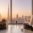 British professional sitting among moving boxes in a Dubai apartment at dawn, planning the first year of a real estate career with the Dubai skyline through floor-to-ceiling glass.